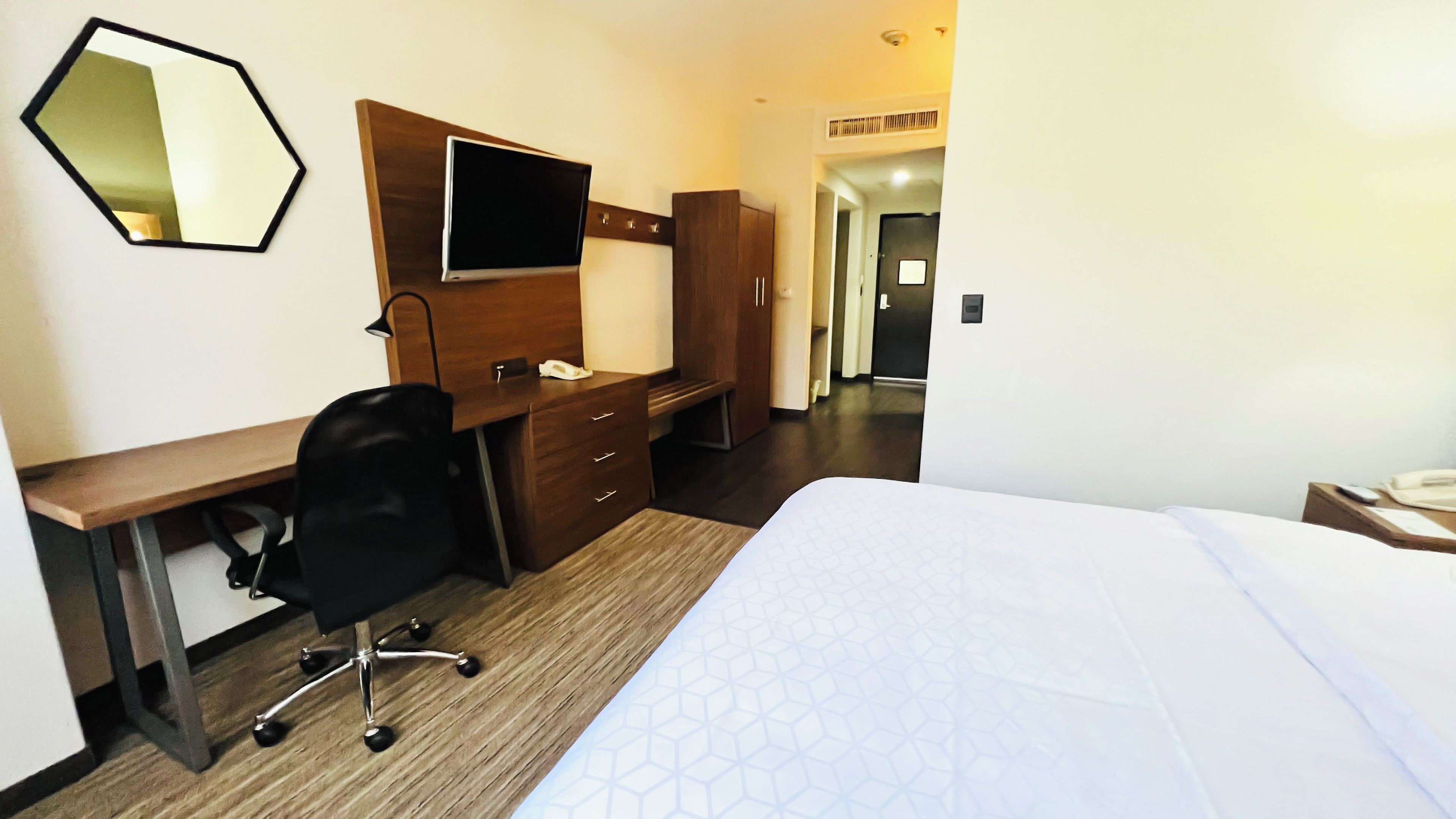 A hotel room with a bed, a desk, a chair, a TV, and a wardrobe.
