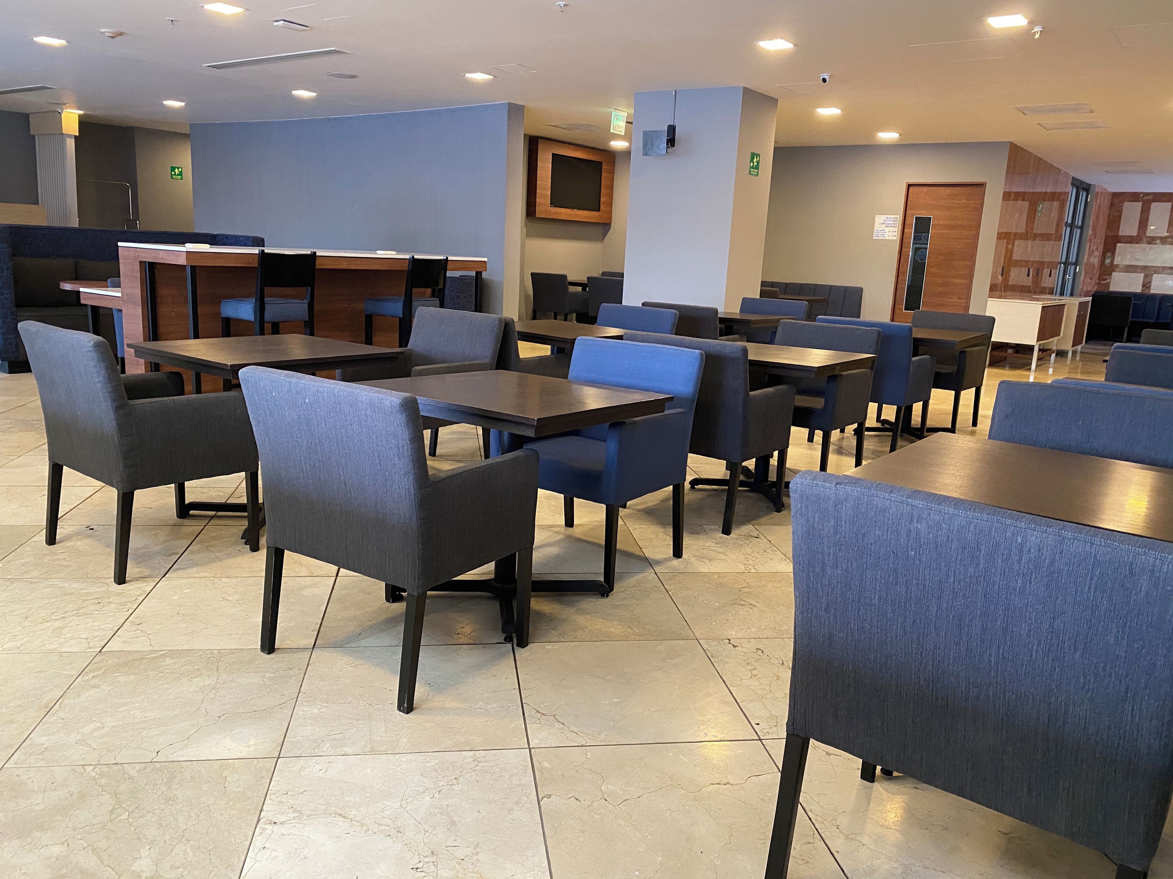 Un restaurant doté de plusieurs tables et chaises, d’un espace cuisine et d’un sol carrelé.