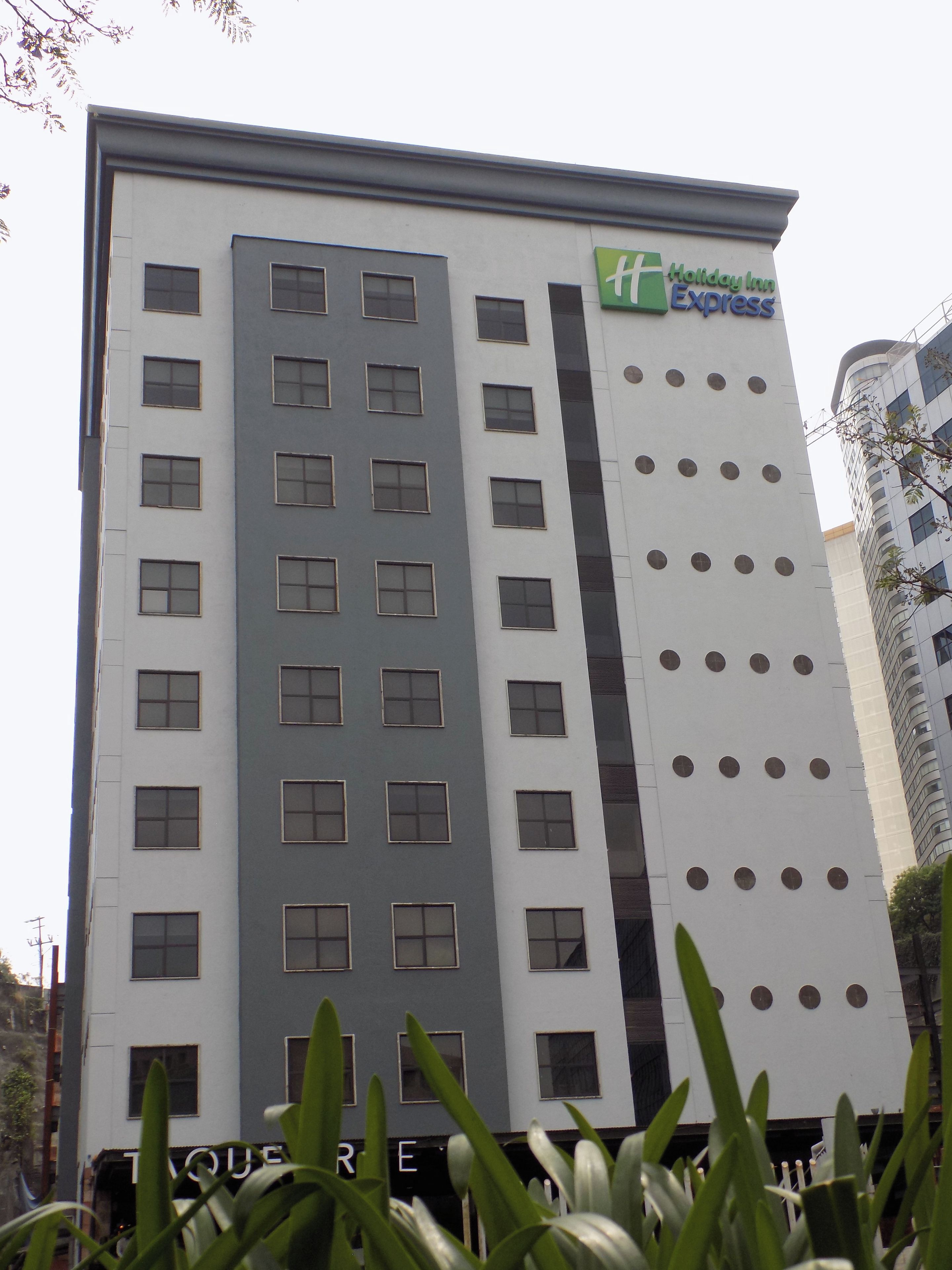 A multi-story building with a Holiday Inn Express sign, featuring a modern design with a mix of window styles and a prominent vertical stripe.