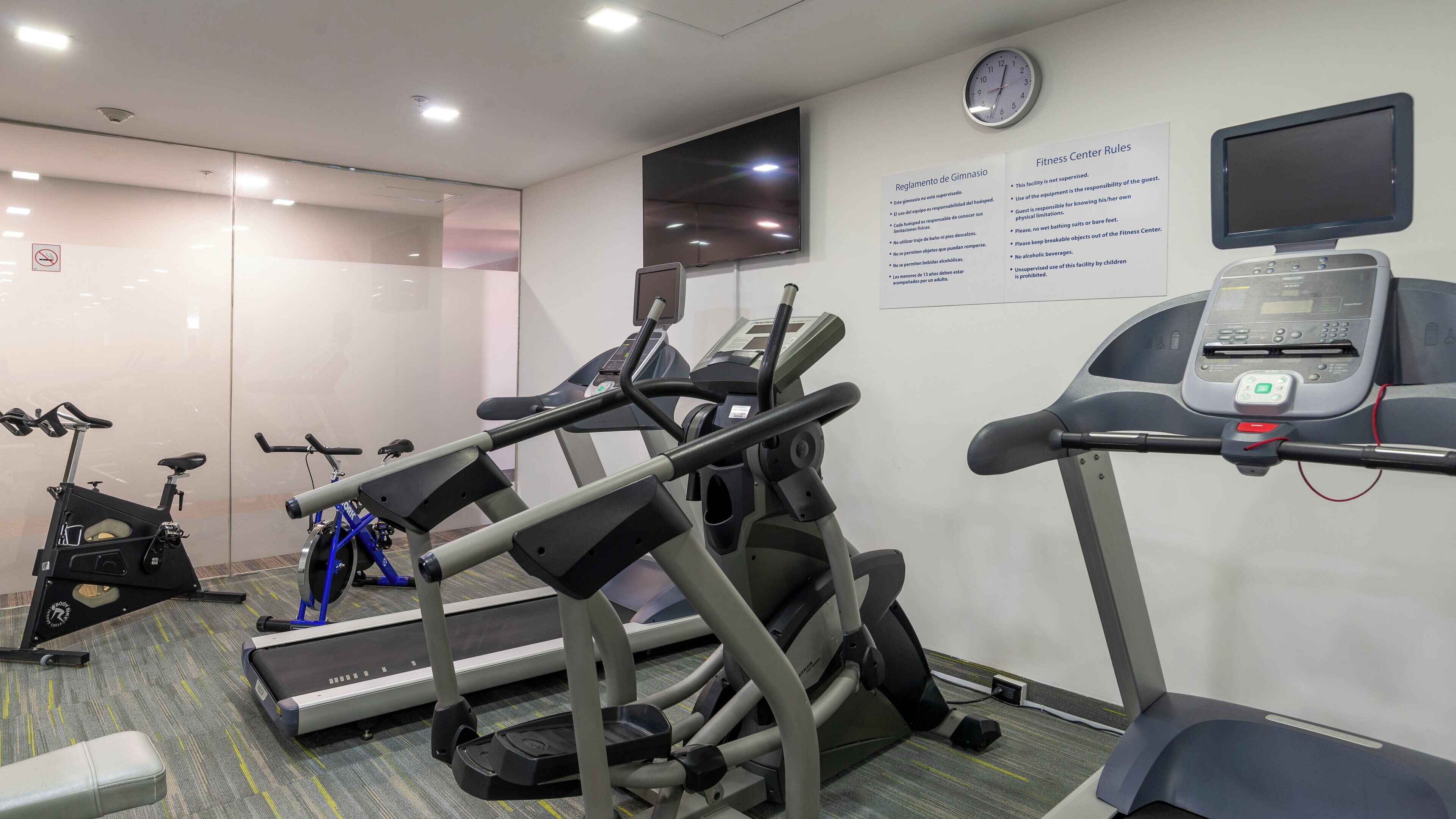 Centro de ginástica com esteiras, bicicletas ergométricas e uma televisão fixada na parede.