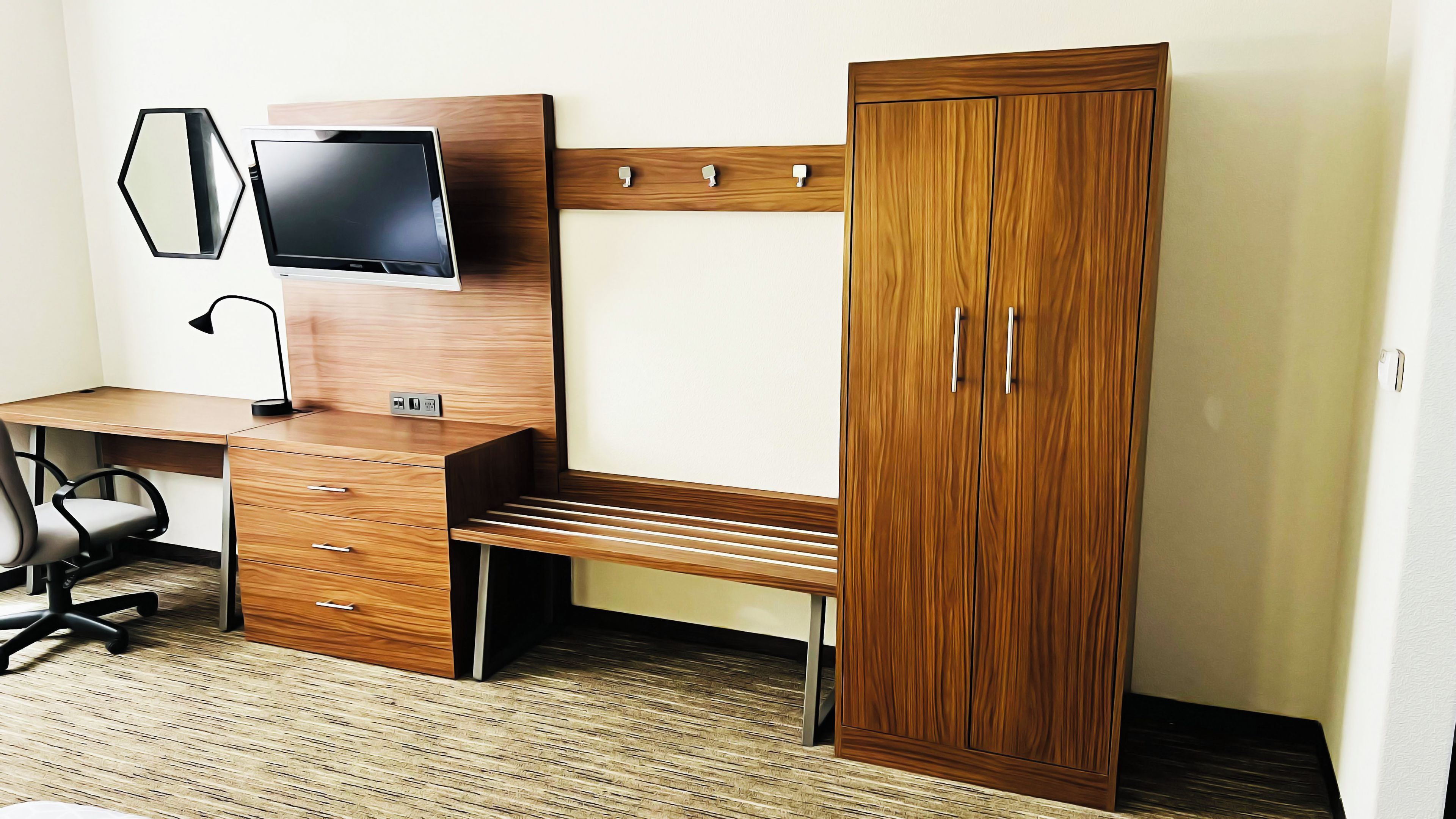 Ein Schlafzimmer mit einem Holztisch, einem Fernseher, einem Kleiderschrank und einem Stuhl.
