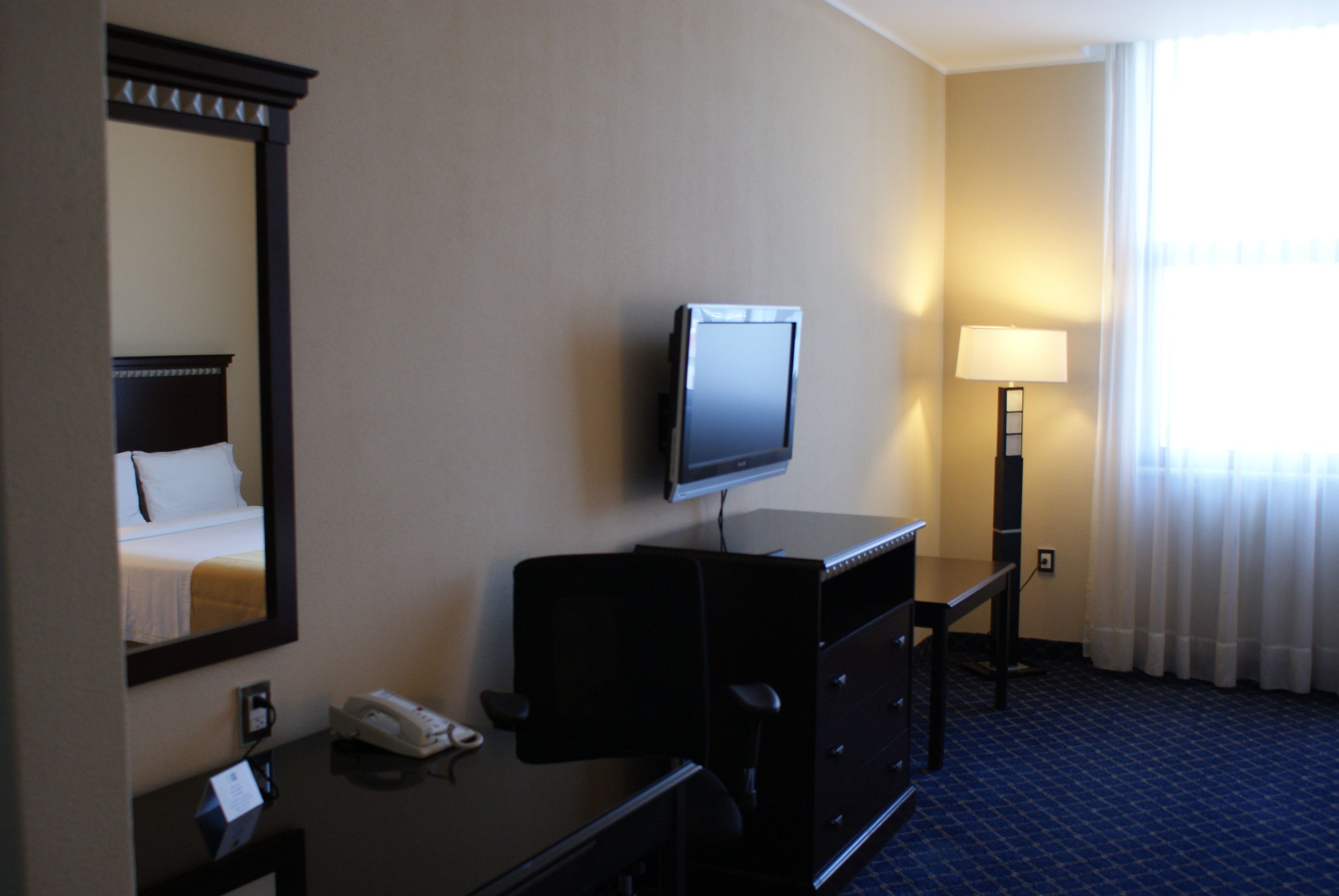 Quarto de hotel com uma cama, uma escrivaninha com telefone, televisão e luminária.