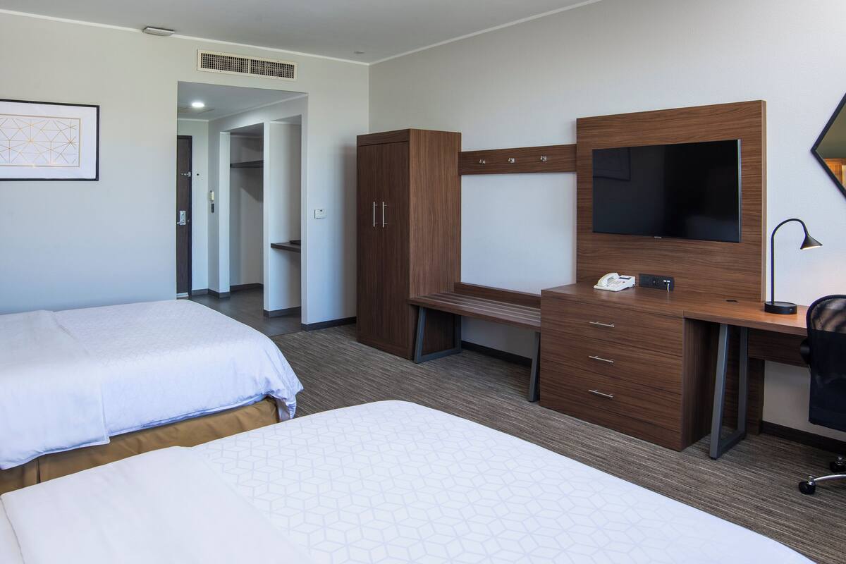 A hotel room with two beds, a desk with a mirror, a chair, and a wardrobe.