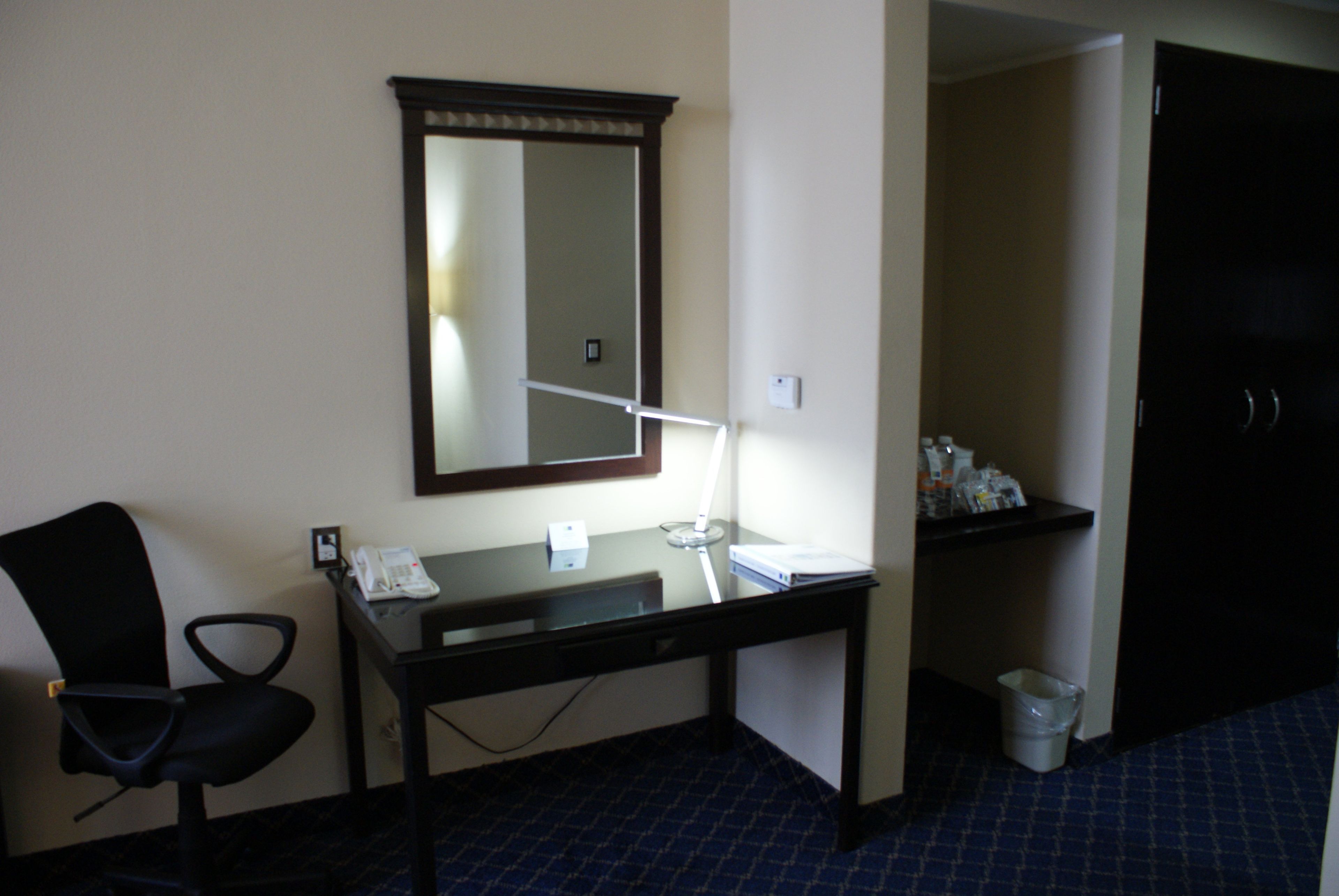 Ein Hotelzimmer mit Schreibtisch, Stuhl, Spiegel und einem kleinen Tisch mit Toiletteartikeln.
