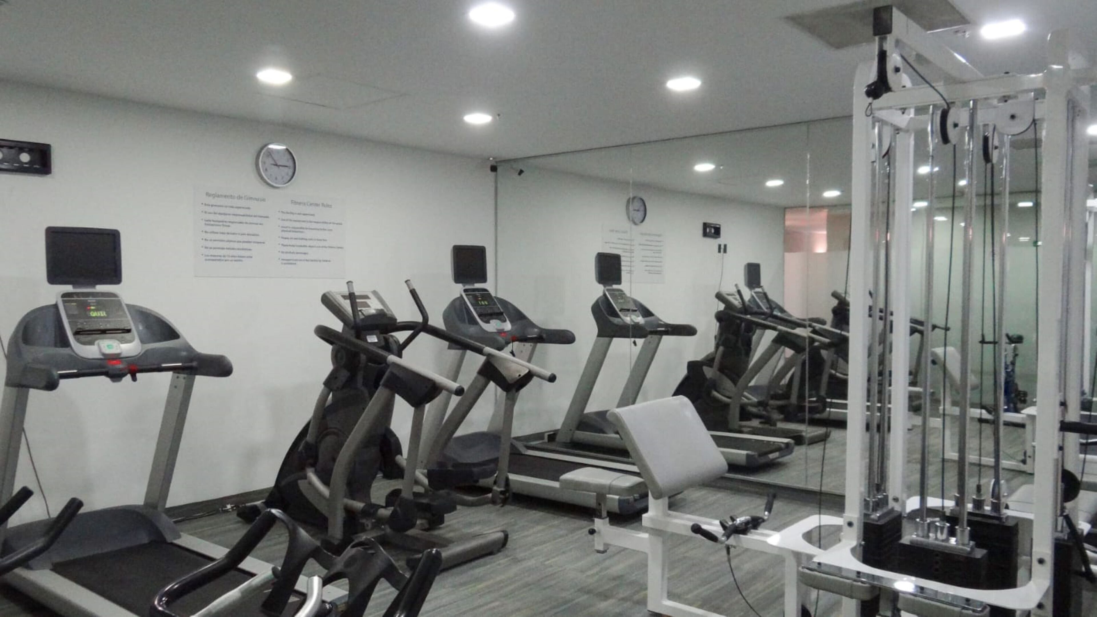 Un gimnasio con cintas de correr, máquinas de pesas y un espejo.
