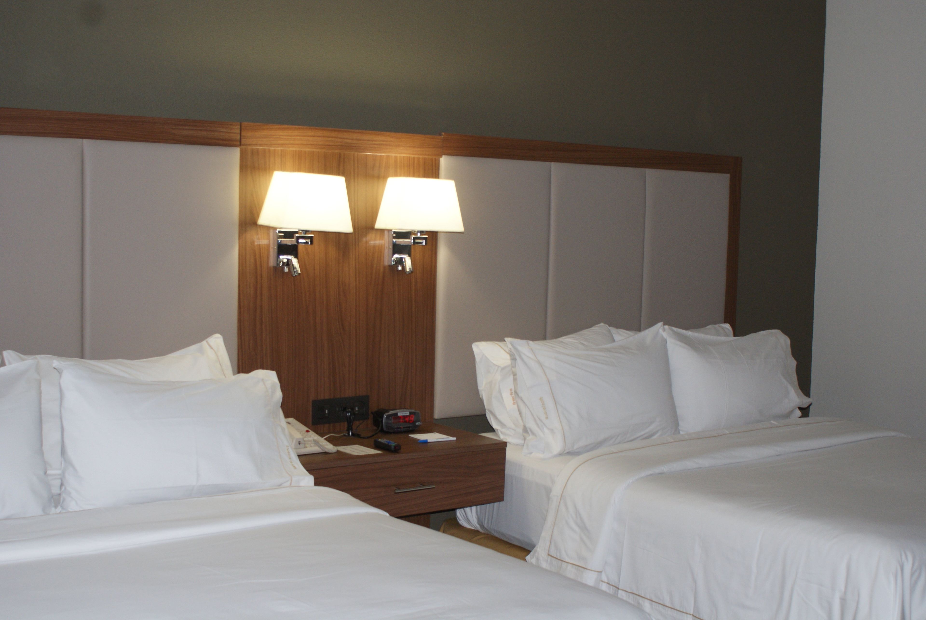 A hotel room with two beds, a nightstand, a clock, and two wall-mounted lamps.