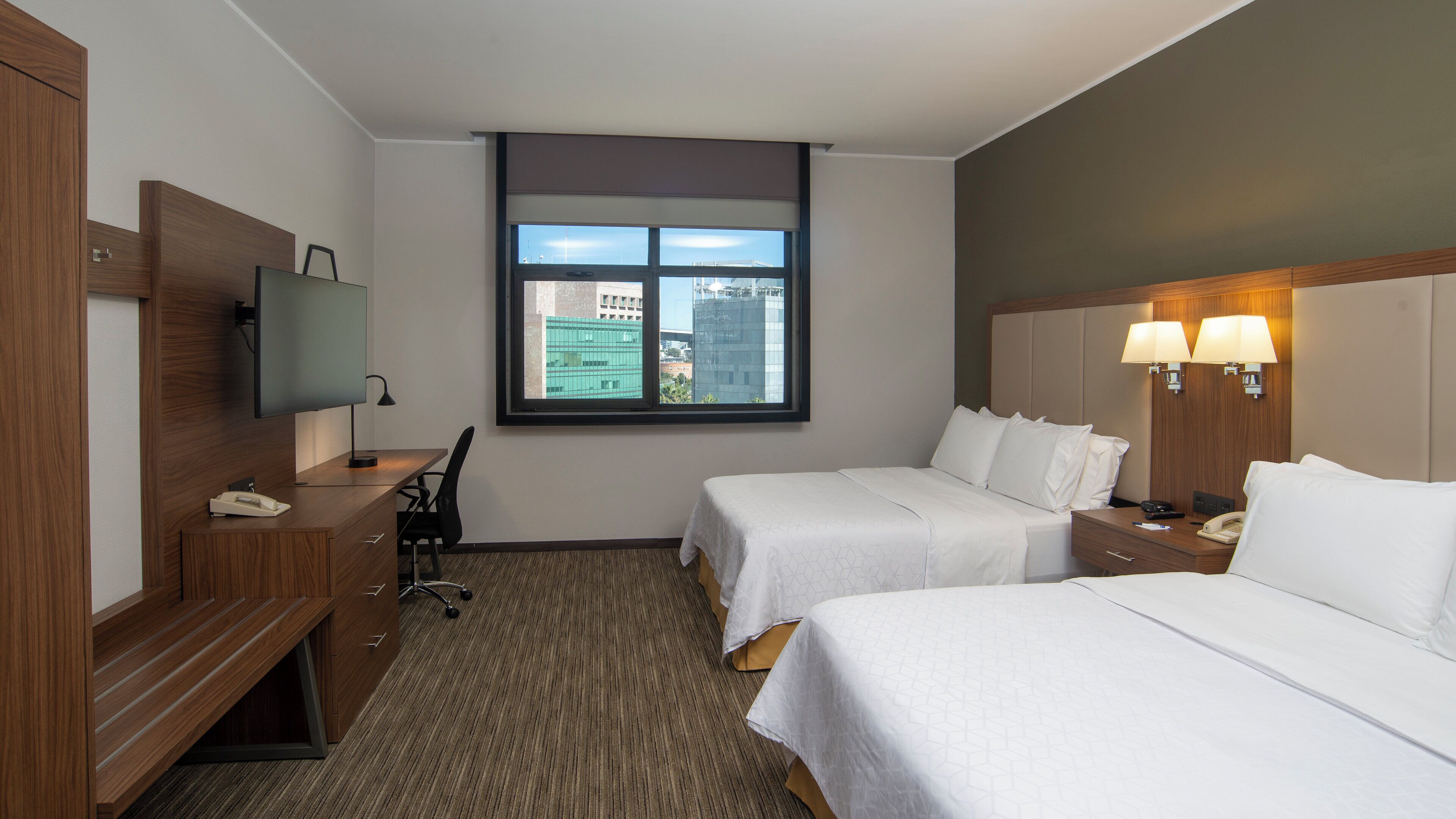 Une chambre d’hôtel avec deux lits, un bureau avec une chaise, une télévision et une fenêtre donnant sur la ville.