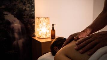 A massage therapy session in a dimly lit room with a statue and a lit lamp in the background.