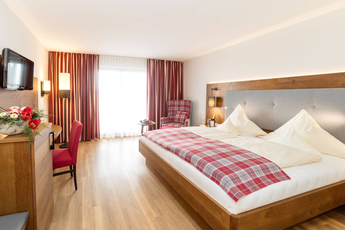 A hotel room with a bed, a desk with a chair, a TV, and a window with curtains.