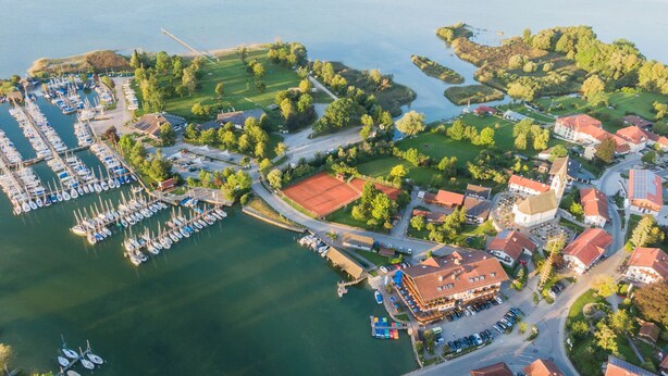 An aerial view of a marina with boats docked, a tennis court, and surrounding residential buildings. - Seehotel Wassermann (Seeon-Seebruck)
