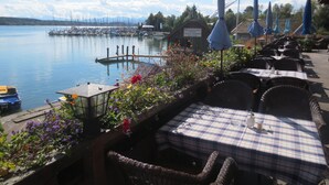 A lakeside restaurant with outdoor seating, a dock, and boats in the background. - Seehotel Wassermann (Seeon-Seebruck)
