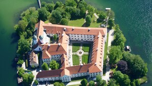 An aerial view of a historic building complex with a central courtyard, surrounded by water and greenery. - Seehotel Wassermann (Seeon-Seebruck)