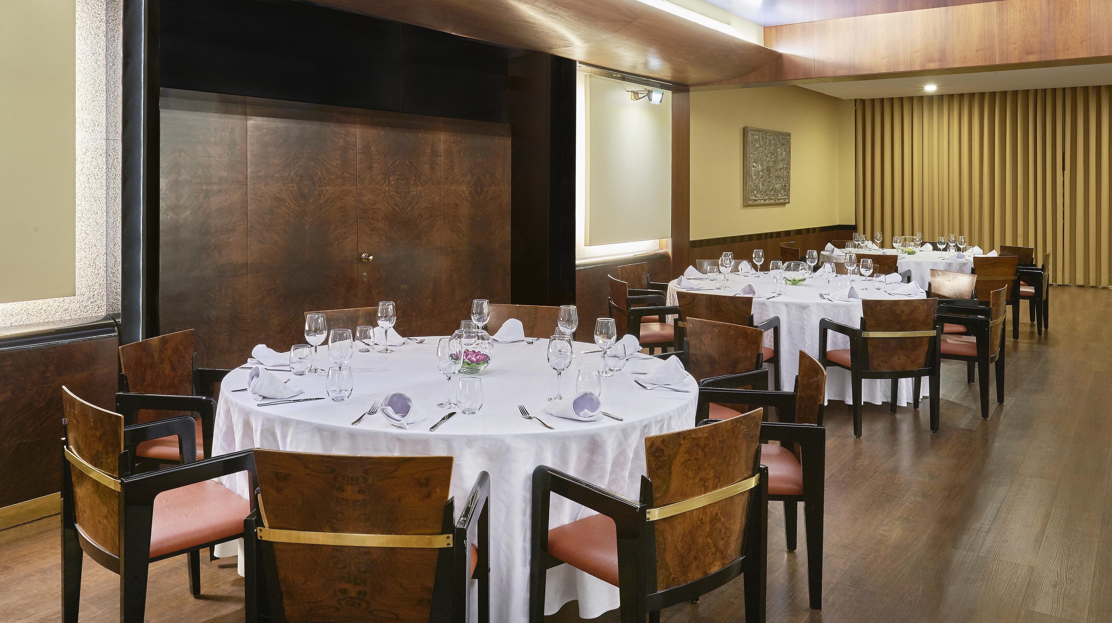 A dining area with round tables set for a meal, each with chairs and table settings.