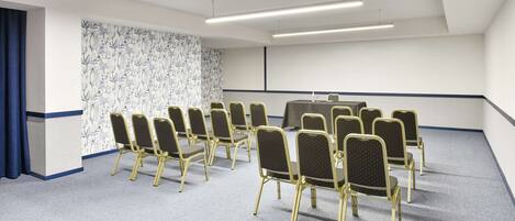 Un salón de conferencias con filas de sillas, una mesa y un papel tapiz decorado.