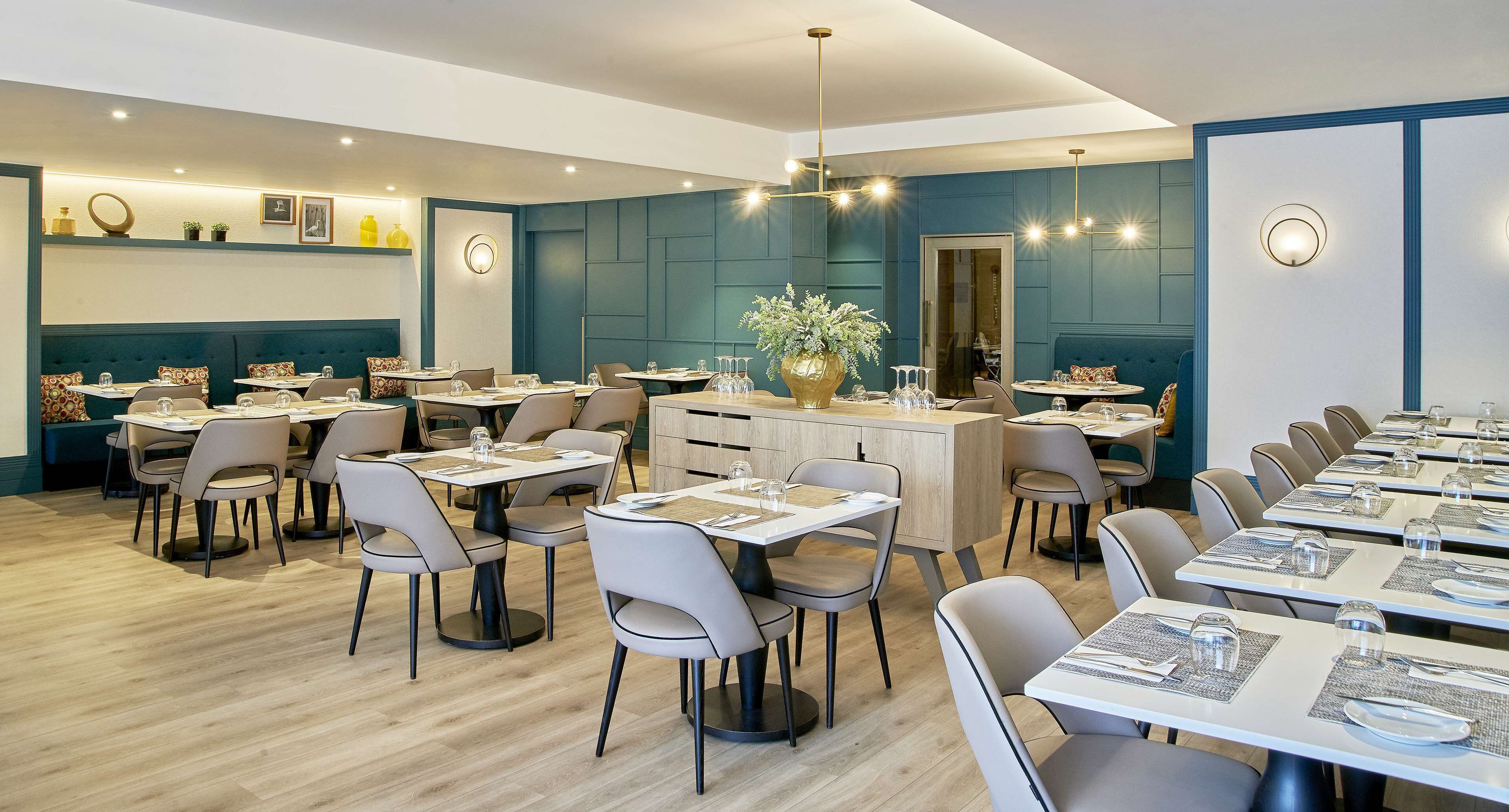 A modern dining area with multiple tables and chairs, a central island with a vase of flowers, and a blue accent wall.