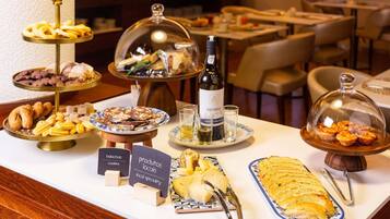 Een buffettafel met diverse gerechten, waaronder gebak, koekjes en kaas, plus een fles wijn.