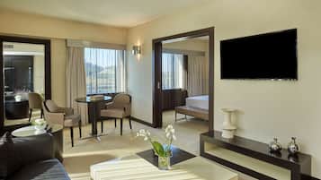 A hotel room with a bed, a TV, a sofa, a coffee table, and a dining area with chairs and a table.