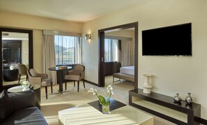 A hotel room with a bed, a TV, a sofa, a coffee table, and a dining area with chairs and a table.