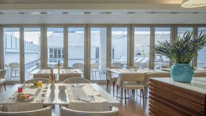 A modern dining area with large windows, white furniture, and a view of the cityscape. - NH Coimbra Dona Inês (Coimbra)