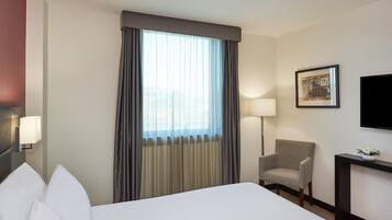 Una habitación de hotel con cama, una silla, un escritorio, una lámpara y un cuadro en la pared.