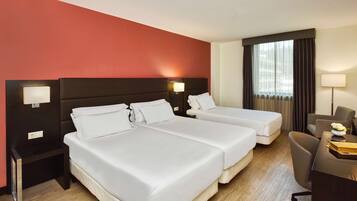 A hotel room with two beds, a desk, a chair, and a window with curtains.