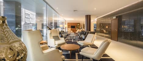 Un vestíbulo de hotel moderno con un área de descanso central, una recepción y un amplio ventanal con vistas a la ciudad.