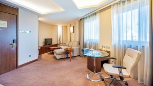 A modern hotel room with a sofa, a glass table, a desk, a chair, a TV, and a large window with curtains. - Grand Skylight Catic Hotel Beijing (Beijing)