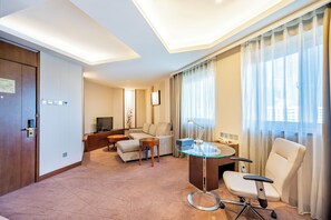 A modern hotel room with a sofa, a glass table, a desk, a chair, a TV, and a large window with curtains. - Grand Skylight Catic Hotel Beijing (Beijing)