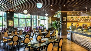 A restaurant with multiple tables and chairs, a bar area with a variety of food items, and large windows allowing natural light. - Grand Skylight Catic Hotel Beijing (Beijing)