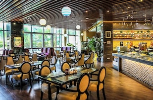 Un restaurante con varias mesas y sillas, una zona de bar con diversas opciones de comida y amplios ventanales que dejan entrar luz natural.