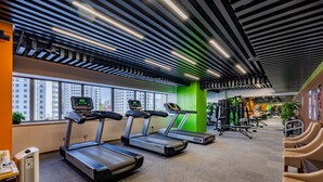 A gym with treadmills, exercise equipment, and a view of buildings through large windows. - Grand Skylight Catic Hotel Beijing (Beijing)