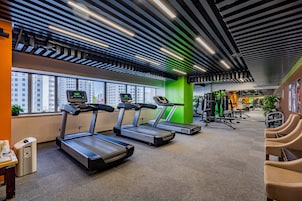 A gym with treadmills, exercise equipment, and a view of buildings through large windows.