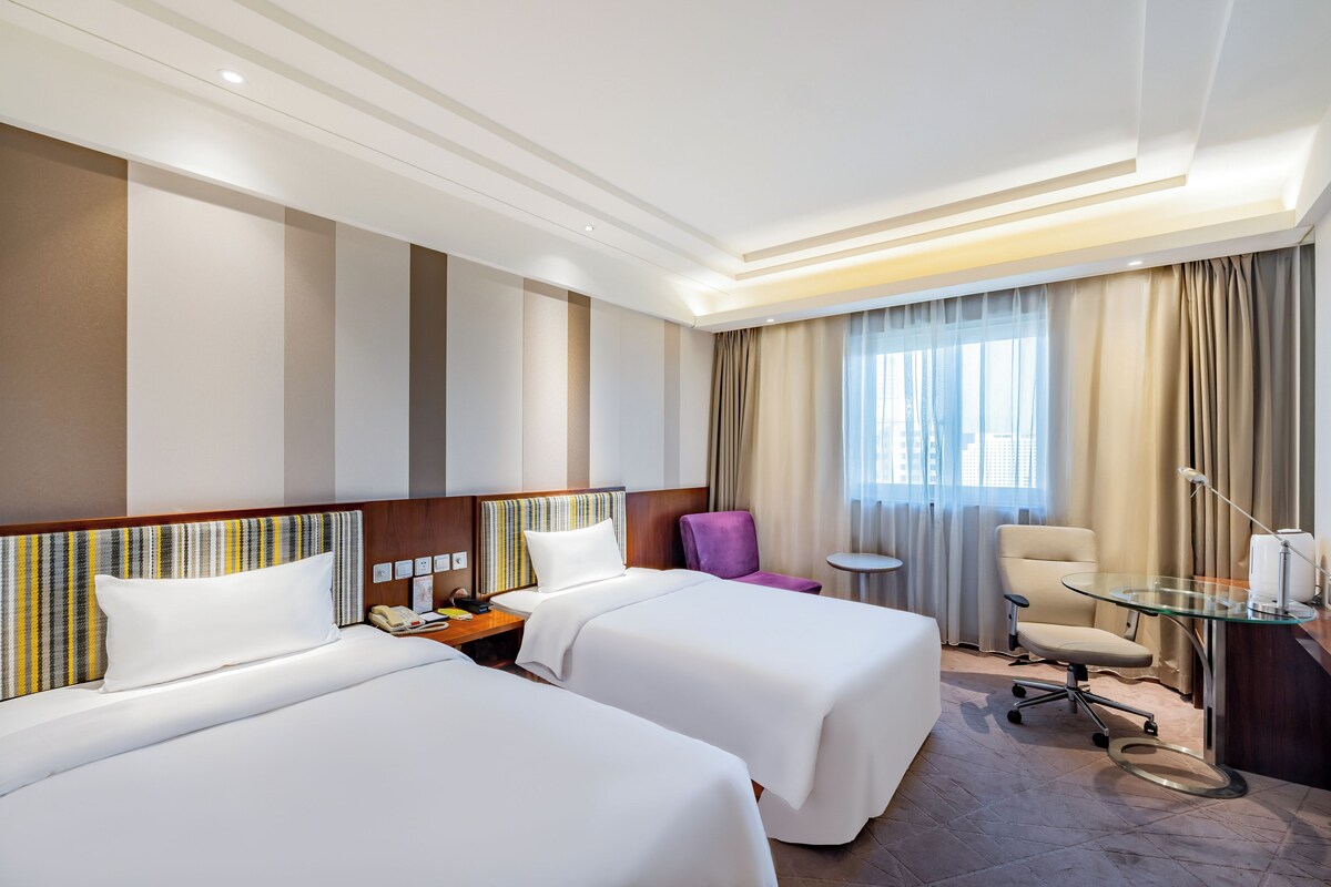Habitación de hotel con dos camas, una mesita, una silla y un escritorio con lámpara.