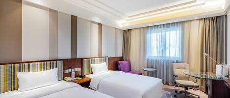 Habitación de hotel con dos camas, una mesita, una silla y un escritorio con lámpara.