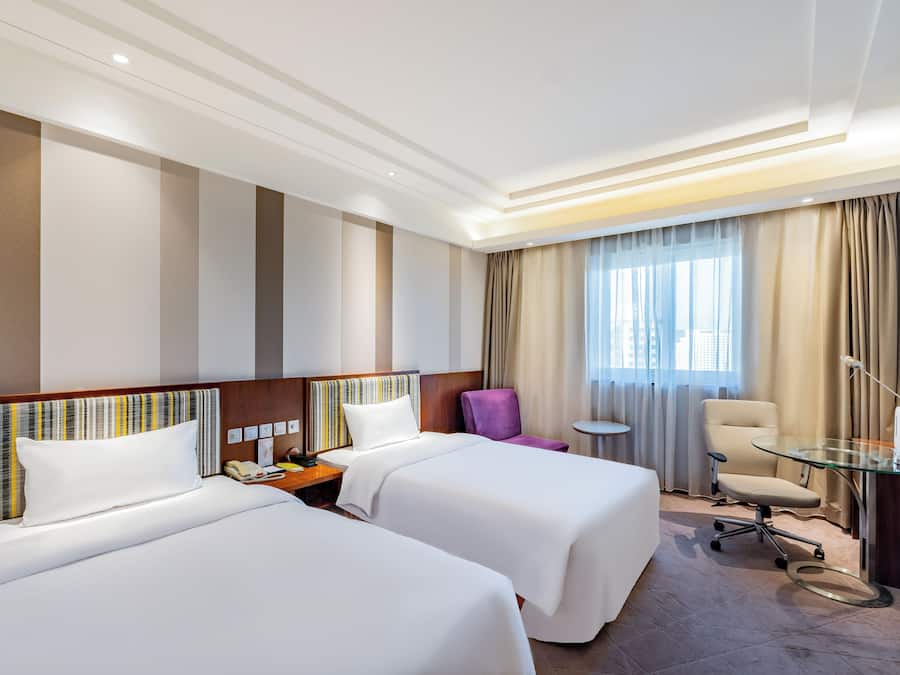Une chambre d’hôtel avec deux lits, une petite table, une chaise et un bureau avec une lampe.