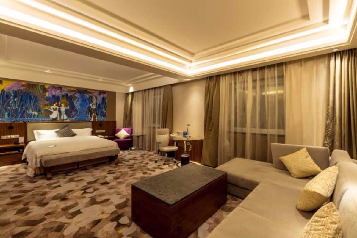 A hotel room with a bed, a sofa, a coffee table, a desk, and a chair.