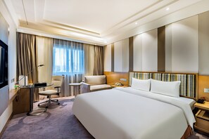 A hotel room with a large bed, a desk with a lamp, a chair, and a small table. - Grand Skylight Hotel Beijing (Beijing)