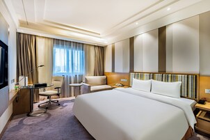Una habitación de hotel con una cama grande, un escritorio con lámpara, una silla y una pequeña mesa.