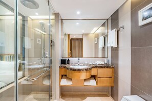 Un baño moderno con ducha envuelta en cristal, tocador de mármol y un espejo grande.