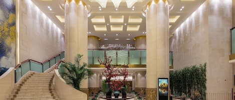 Um hall amplo com uma escadaria imponente, um arranjo floral decorativo central e um lustre moderno.