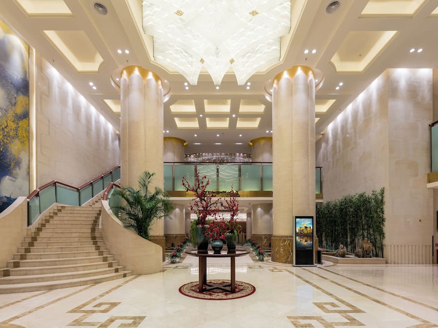 A spacious lobby with a grand staircase, a central decorative plant arrangement, and a modern chandelier.