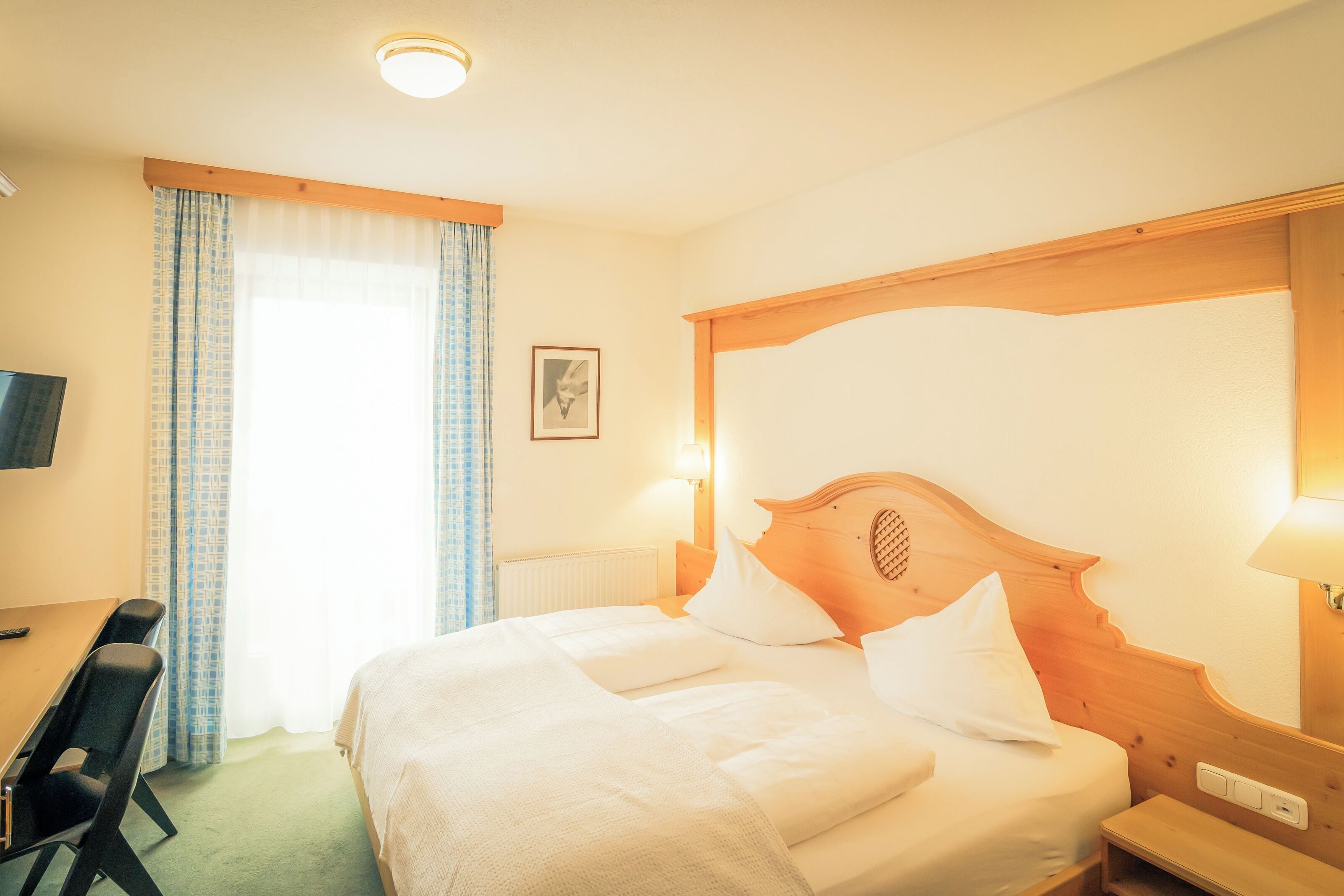 Une chambre d’hôtel avec un lit, un bureau, une chaise, une télévision et une fenêtre avec des rideaux.