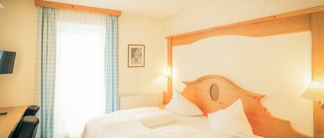 A hotel room with a bed, a desk, a chair, a TV, and a window with curtains.