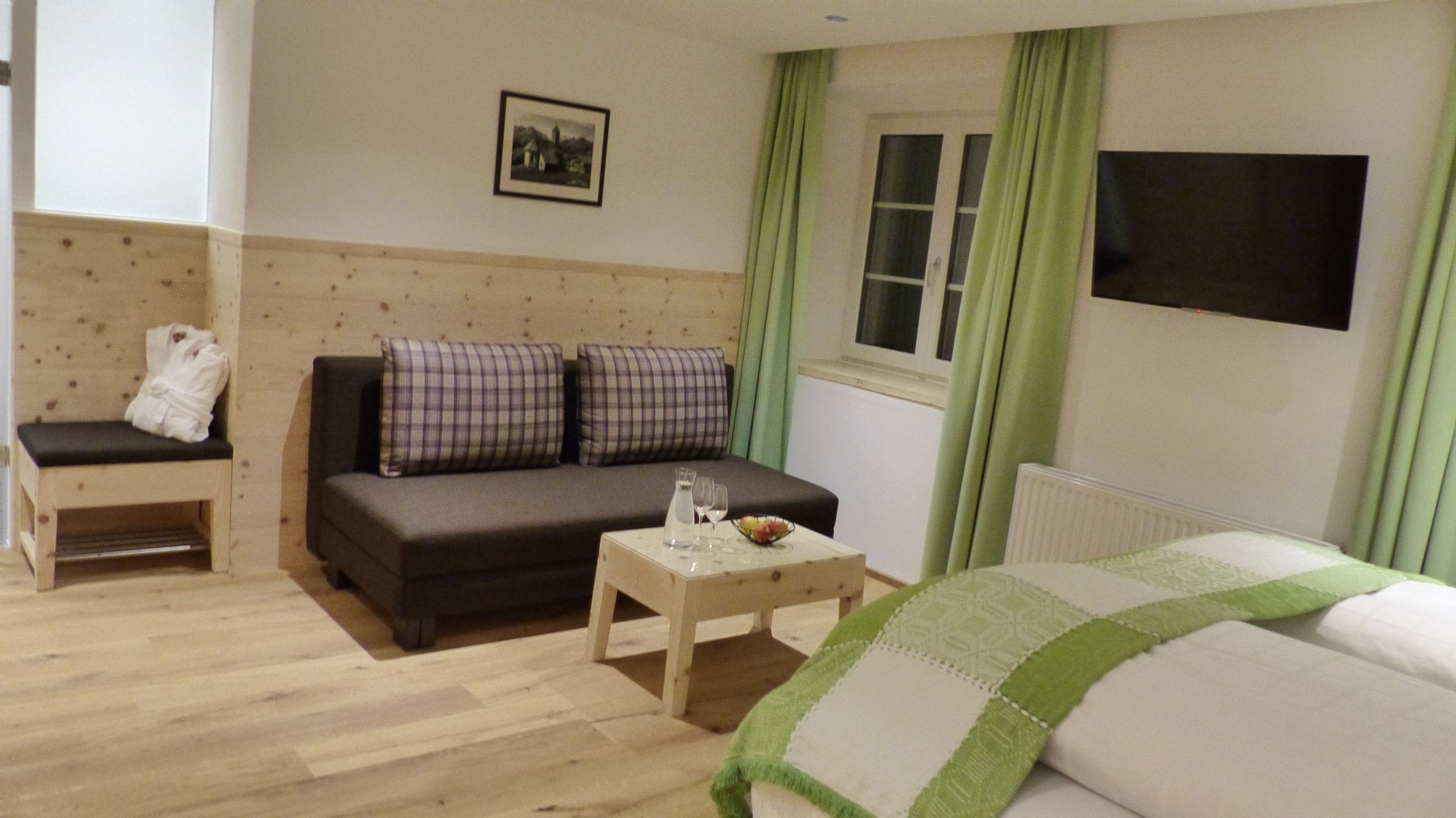 Ein gemütliches Zimmer mit einer Couch, einer Bank, einem kleinen Tisch mit Obstschale und einem Bett.