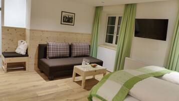 A cozy room with a sofa, a bench, a small table with a bowl of fruit, and a bed.