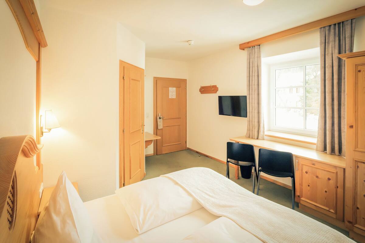 A hotel room with a bed, a desk with two chairs, a television, and a window with curtains.