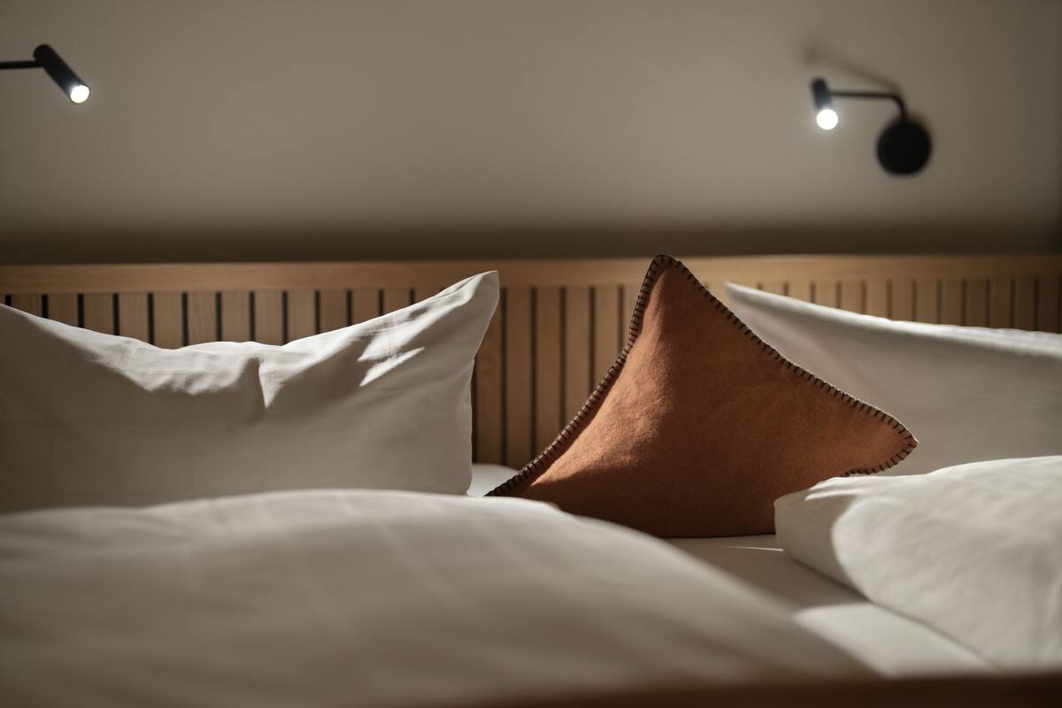 A neatly made bed with white and brown pillows, a wooden headboard, and two wall-mounted reading lamps.