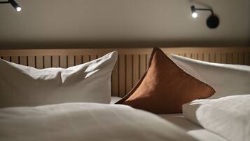 A neatly made bed with white and brown pillows, a wooden headboard, and two wall-mounted reading lamps.