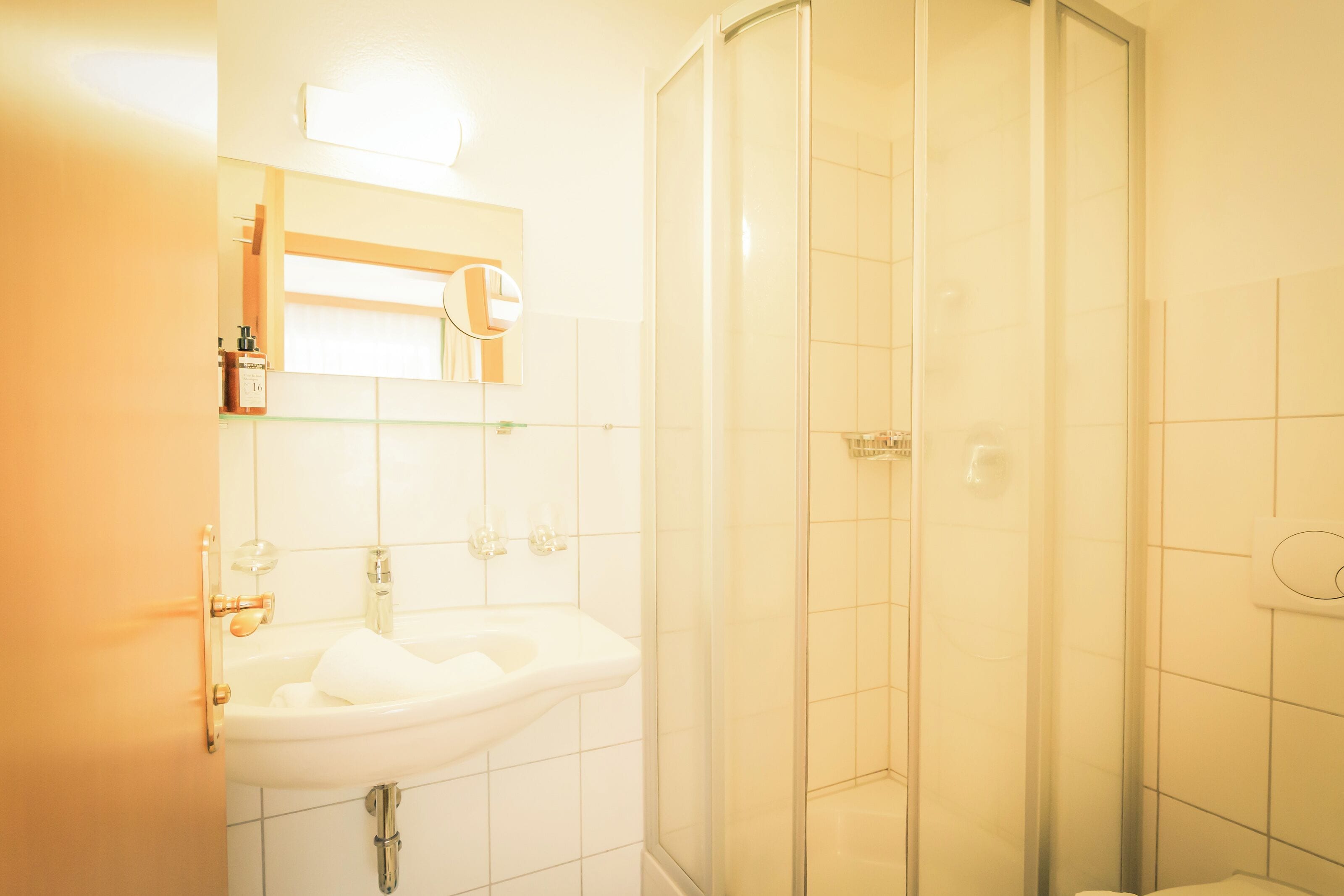 Un baño con un lavabo blanco, una cabina de ducha de vidrio y un espejo sobre el lavabo.