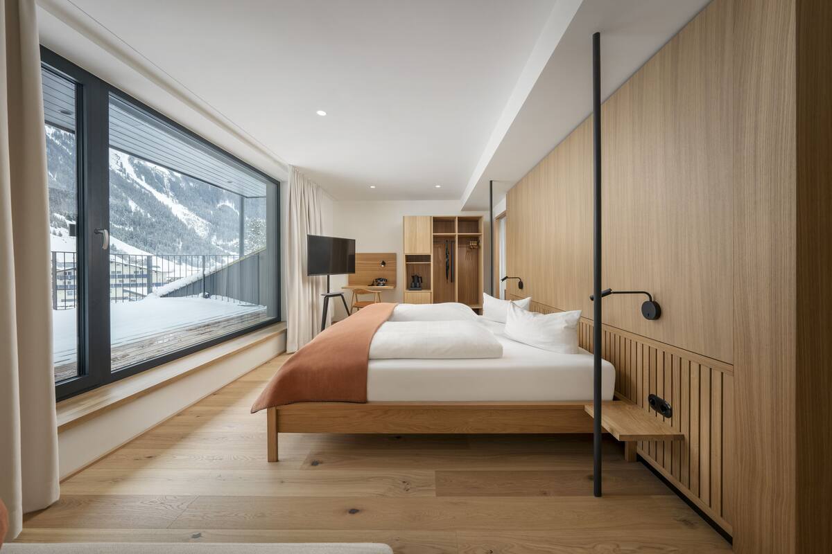 A modern bedroom with a large window, a bed, a bedside table, and a wardrobe.